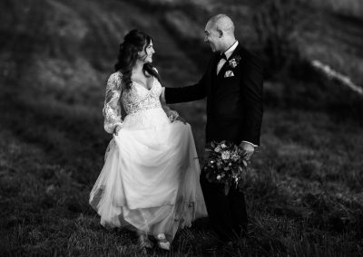 Black and white image of bride and groom walking across fields in the Cotswolds